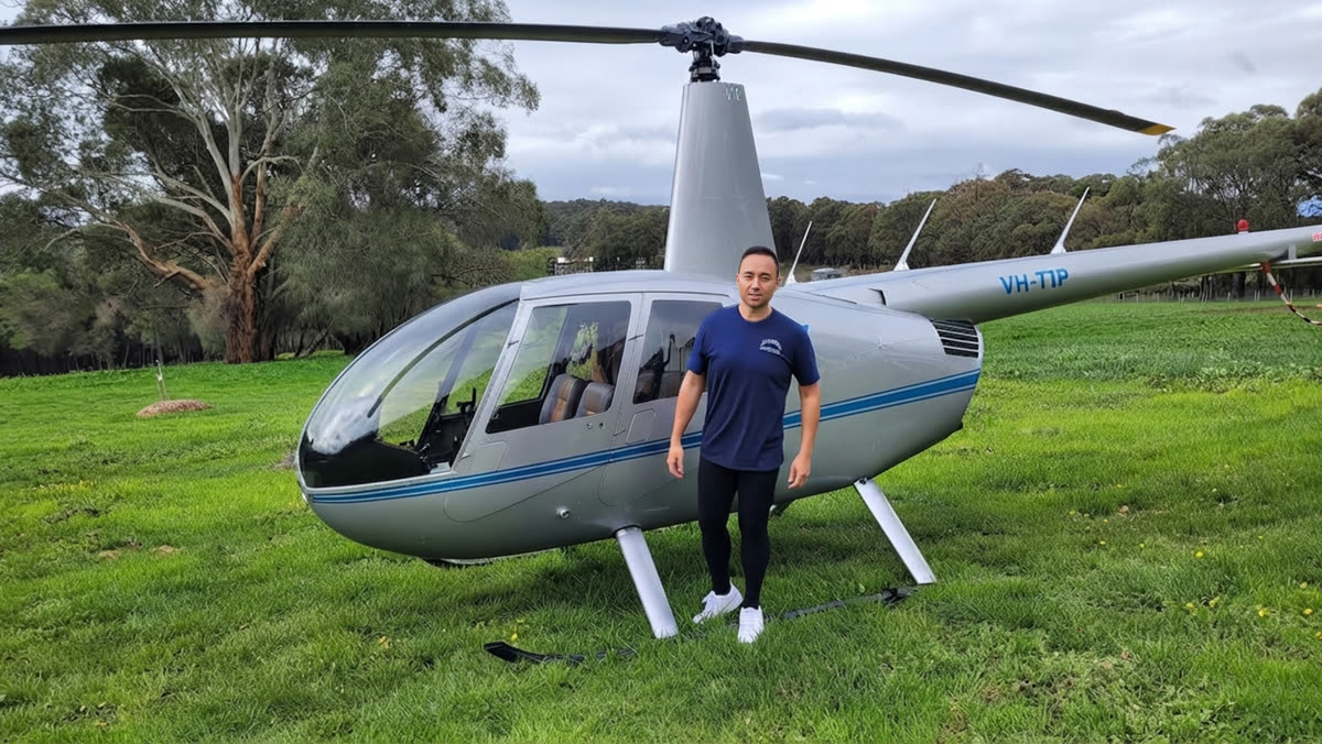 Matt standing in front of an R44 helicopter on his farm